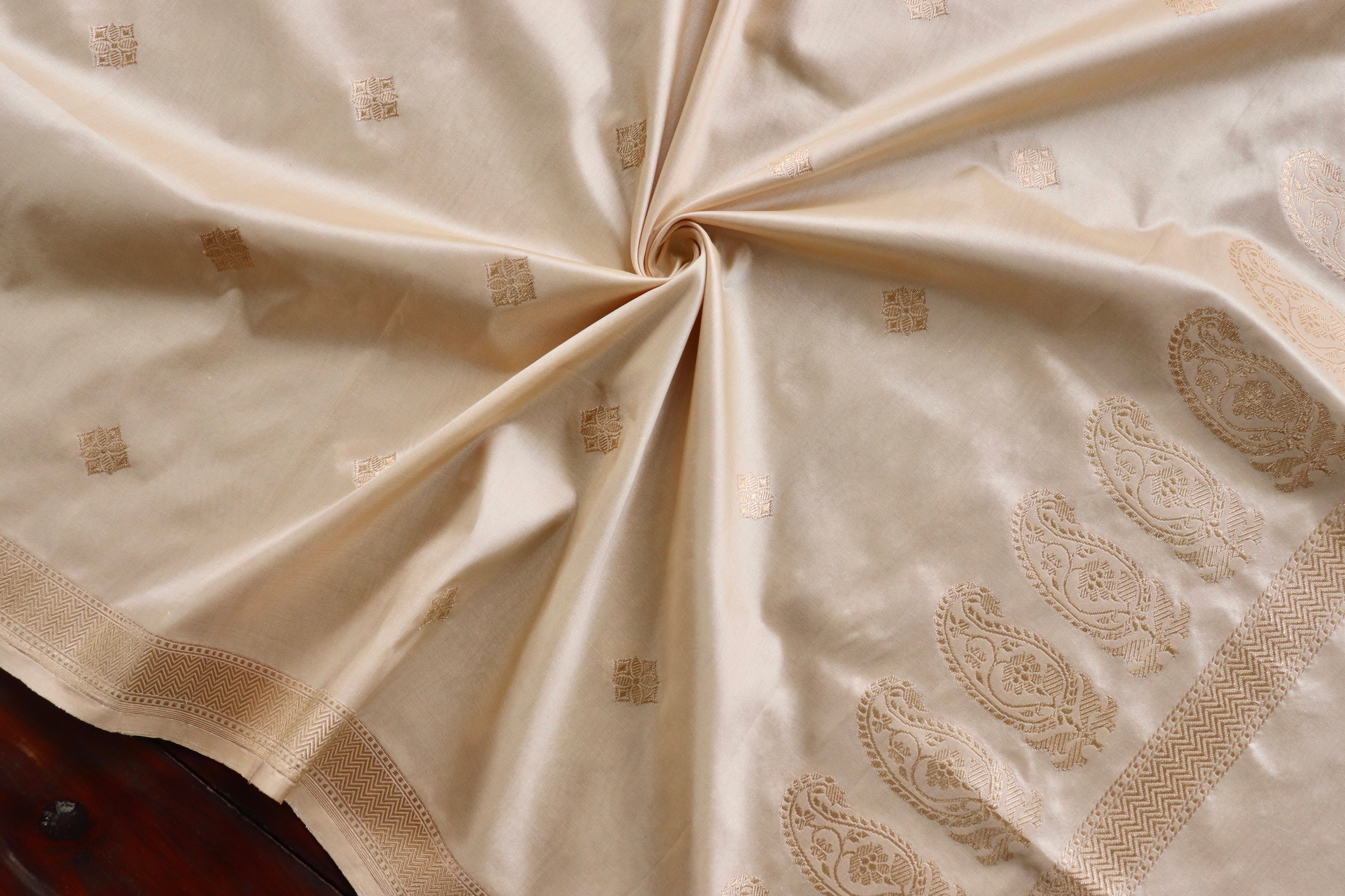 A cream Banarasi arranged in a soft swirl, its woven kalga motifs catching the light
