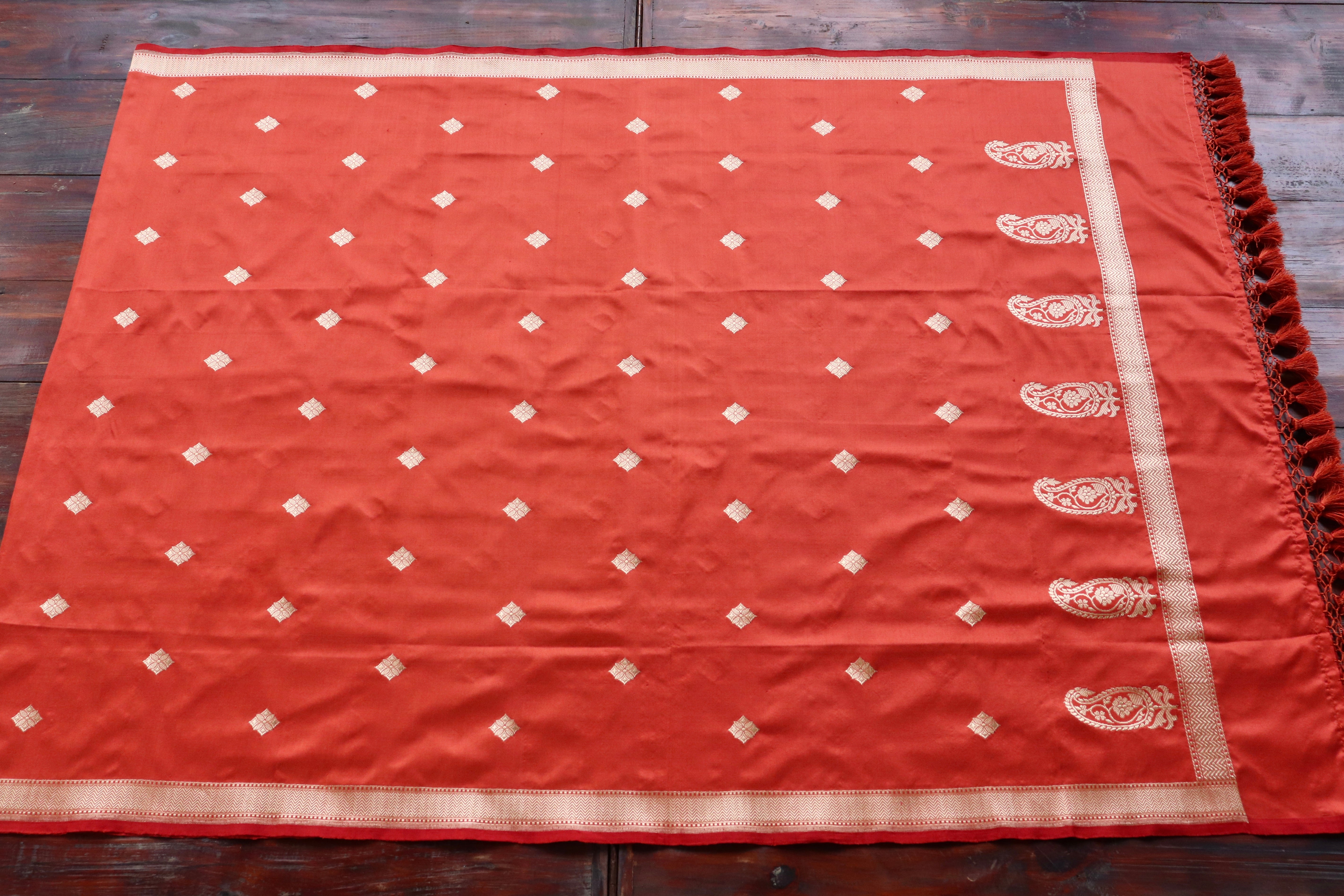 An orange handloom Banarasi spread flat, its gold field catching the light